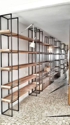 an empty room with shelves and ladders on the wall, next to a brick floor