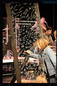 a young child writing on a blackboard in front of other children at a stage