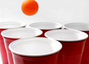 red cups with white rims and an orange ball in the air above them, all lined up