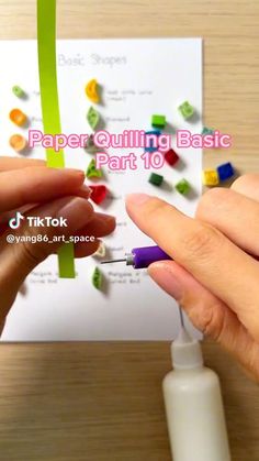 two hands are holding a piece of paper with colored beads on it and one hand is using a glue pen