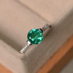 This ring features a 7mm round cut lab emerald and sterling silver finished with rhodium. Customization is available. It is made by hand, and it will take about 7 days to finish the ring after your payment is completed. Main stone: lab emerald Main stone weight: Approx 1.10 ct Metal type: sterling silver finished with rhodium Accent stone: cz Customization is available, I also can make it with 14k solid gold (white or yellow or rose) and diamond accent stone, just feel free to contact me. Any qu Classic Solitaire Emerald Promise Ring, Classic Emerald Promise Ring With Birthstone, Classic Emerald Diamond Promise Ring, Classic Emerald Diamond Ring With Accent Stones, Elegant Green Topaz Ring In Sterling Silver, Elegant Green Topaz Promise Ring, Classic Solitaire Diamond Ring For May Birthstone, Classic Diamond Ring With Accent Stones For May Birthstone, Fine Jewelry Emerald Promise Ring With Center Stone