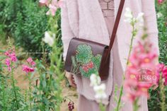 a woman is standing in the middle of flowers with her hand on her hip bag