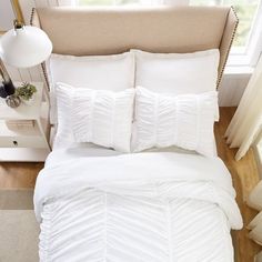 a bed with white comforter and pillows in a small room next to a window