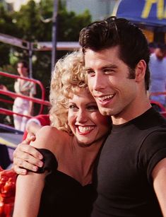 a man and woman hugging each other in front of an amusement park area with people watching