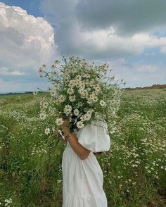 a woman in a white dress holding a bouquet of daisies