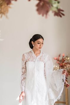 a woman standing in front of a white wall wearing a white dress with sheer sleeves