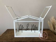 a white glass house with mr and mrs written on the front window, sitting on top of a wooden table