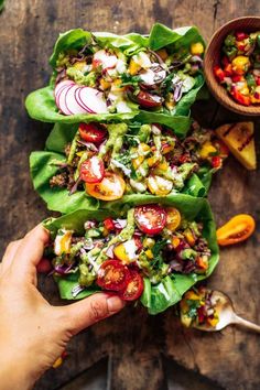 a person is holding up some lettuce wraps with tomatoes and other toppings