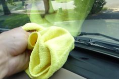 a person wiping the inside of a car window with a yellow microfiber cloth