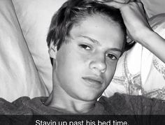 a black and white photo of a boy laying in bed with his hand on his head