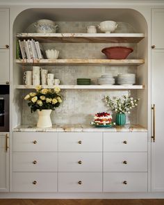 a kitchen with white cupboards and shelves filled with plates, cups, bowls and vases