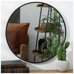 a round mirror sitting on top of a wooden table next to a potted plant