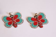 two pairs of colorful beaded butterfly earrings on a white surface, one with red and blue beads