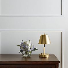 a table with a lamp, vase and flowers on it next to a white wall