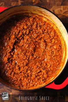 a large pot filled with chili sauce on top of a wooden table next to a red spatula