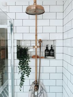 a bathroom with white tiles and a gold faucet in the shower head next to a green plant