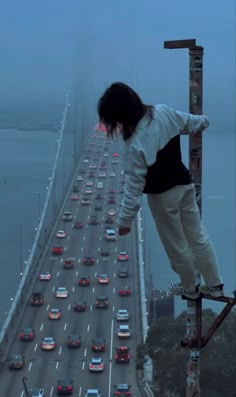 a person on a skateboard is standing on the edge of a high bridge with cars going over it