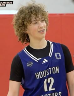 a young man with curly hair wearing a blue uniform and holding a white frisbee