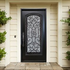 a black iron door in front of a white house with potted plants on either side