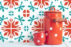 an orange pot and two red polka dot mugs are on the floor in front of a colorful wallpaper