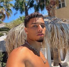 a man with no shirt standing in front of a palm tree and thatched umbrella