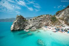 an aerial view of the beach with umbrellas and people swimming in clear blue water