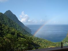 a rainbow is seen over the ocean from a balcony in front of a mountain range