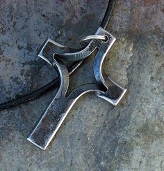 a silver cross on a black leather cord laying on the ground next to some rocks