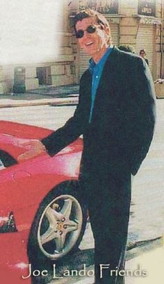 a man standing next to a red sports car in front of a building with the words joe lando friends written on it