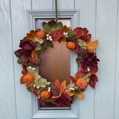 a wreath is hanging on the front door with autumn leaves and pumpkins around it