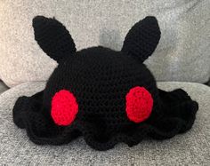 a crocheted black hat with red eyes is sitting on a gray sofa cushion