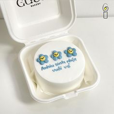 a white cake in a plastic container with two blue monkeys on it's side