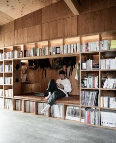 a man sitting on top of a wooden shelf filled with books