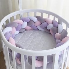 a white crib with pink, purple and grey pillows in it's center