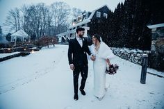 a bride and groom are walking through the snow in front of a house on their wedding day