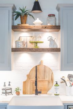 a kitchen sink with wooden cutting board and utensils on the shelf above it