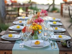 a long table is set with flowers and wine glasses for an outdoor dinner party or celebration