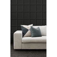 a couch with two pillows on it in front of a black wall and grey carpet