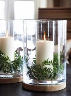 two glass vases with candles and greenery in them