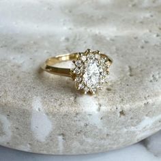 a diamond ring sitting on top of a white marble slabd surface, with the center stone surrounded by smaller round diamonds