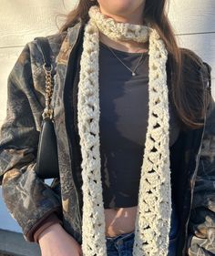 a woman wearing a white crochet scarf and black leather jacket standing in front of a wall