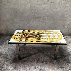 a glass table with yellow and black designs on the top, against a concrete wall