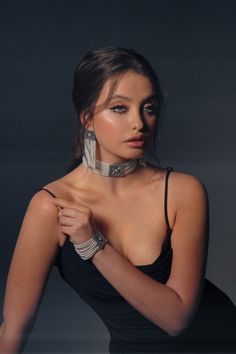 a woman in a black dress with silver jewelry on her neck posing for the camera