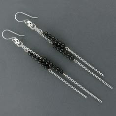 three pairs of black beaded earrings with silver chains hanging from them on a gray surface