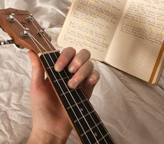 a person holding an ukulele in their left hand and open book on the bed