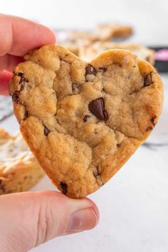 someone holding up a heart shaped chocolate chip cookie