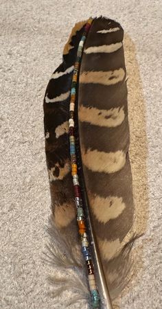 a feather with beads and a beaded necklace on it's end laying on the ground