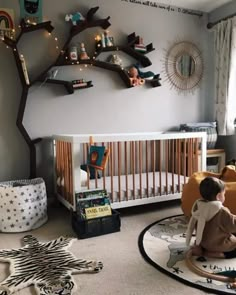 a baby sitting in a crib next to a tree with lights on the branches