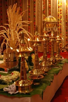 a table topped with lots of gold vases filled with flowers and candles on top of it