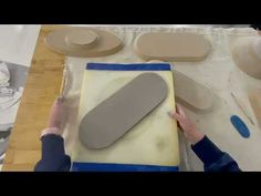 a woman is working with clay on a piece of paper that has been cut into shapes